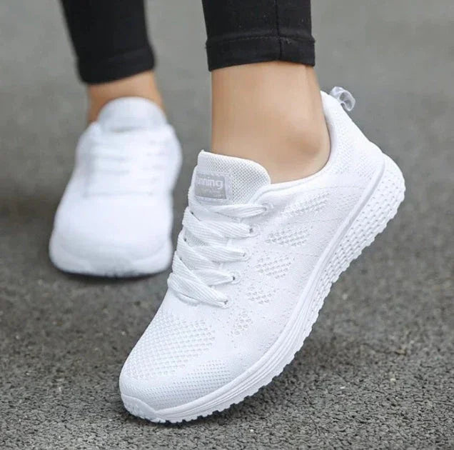 White athletic running shoes with mesh upper worn on pavement