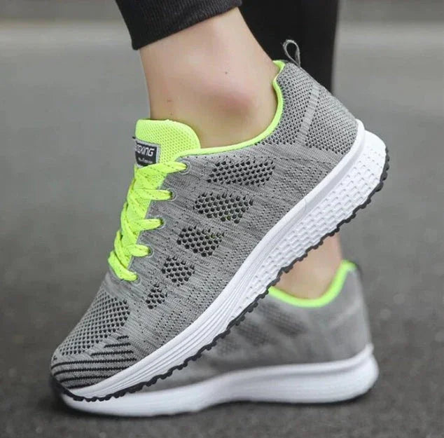 Gray athletic running shoes with neon yellow accents and mesh upper on pavement