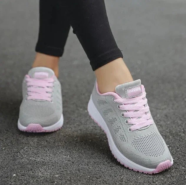 Gray and pink athletic running shoes worn on pavement, mesh upper, lace-up design.