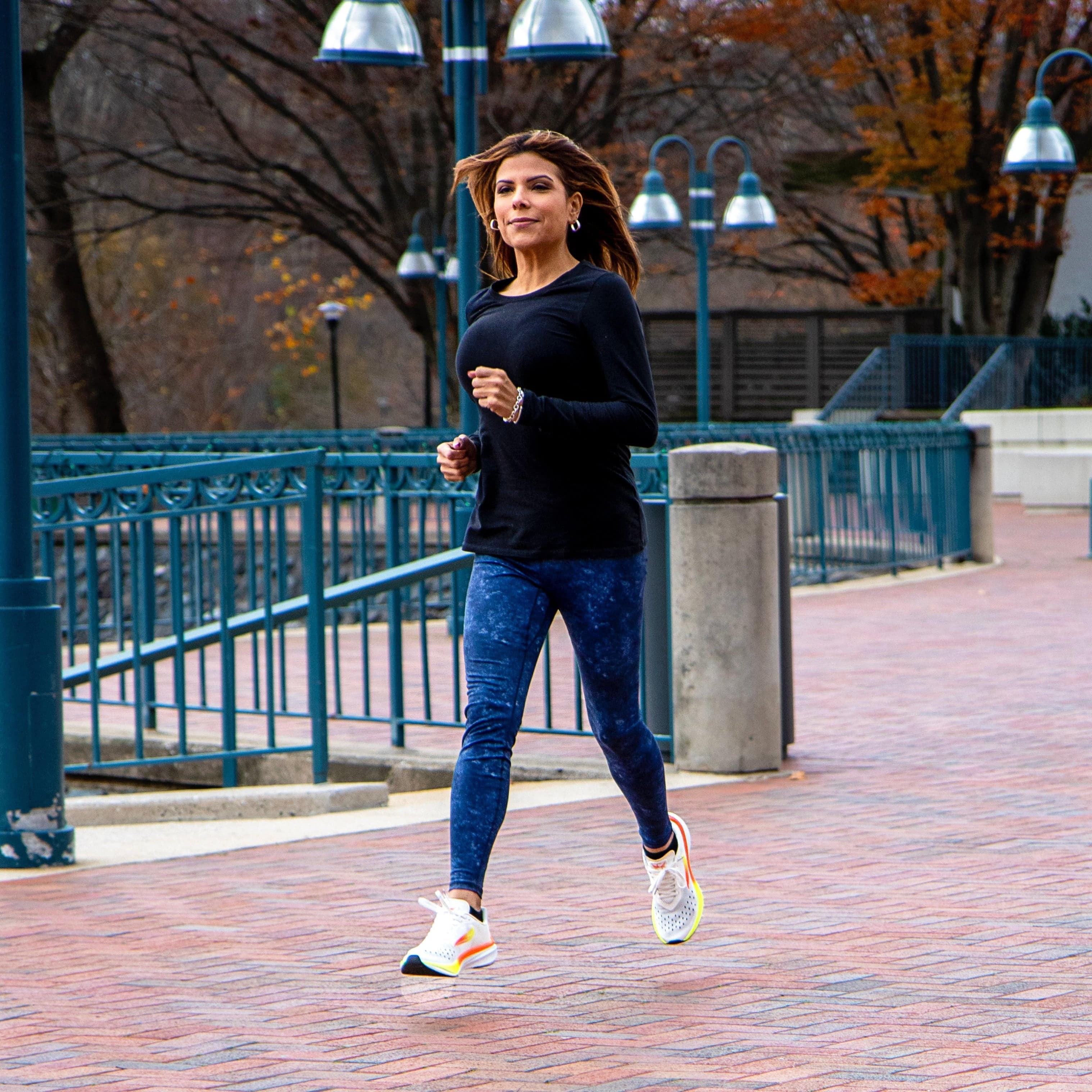 Woman jogging outdoors in athletic running shoes, blue leggings, and black top on a brick path