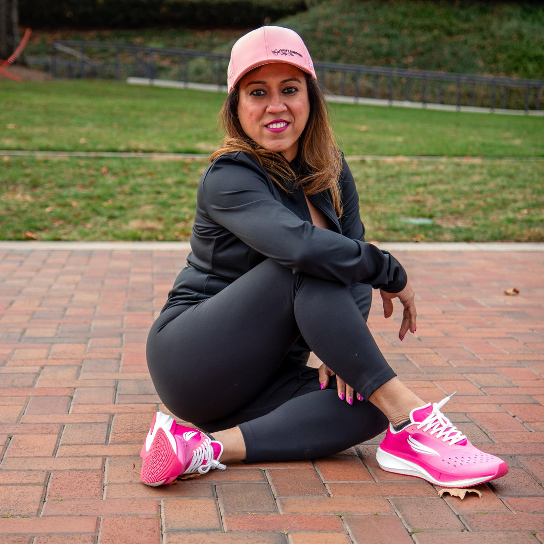 Woman sitting outdoors in pink running shoes and activewear on a brick path