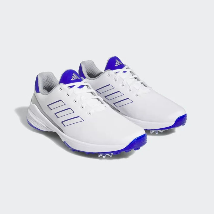 White athletic golf shoes with blue accents and spike soles on a plain background