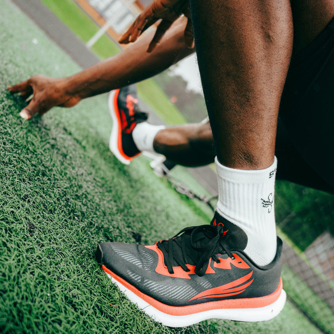 Athlete wearing black and red running shoes on track, preparing to sprint