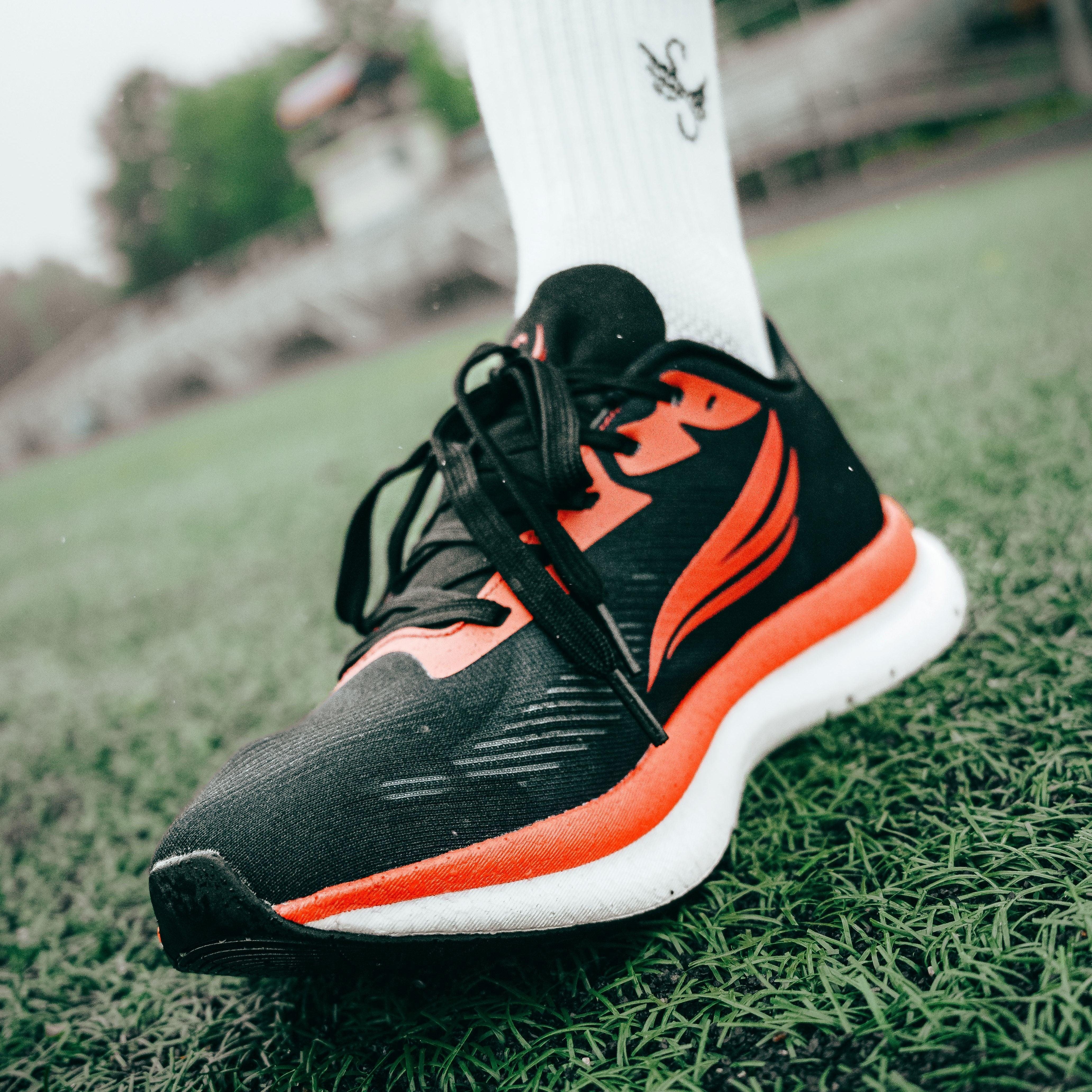 Black and orange athletic running shoe on foot, close-up on green turf field