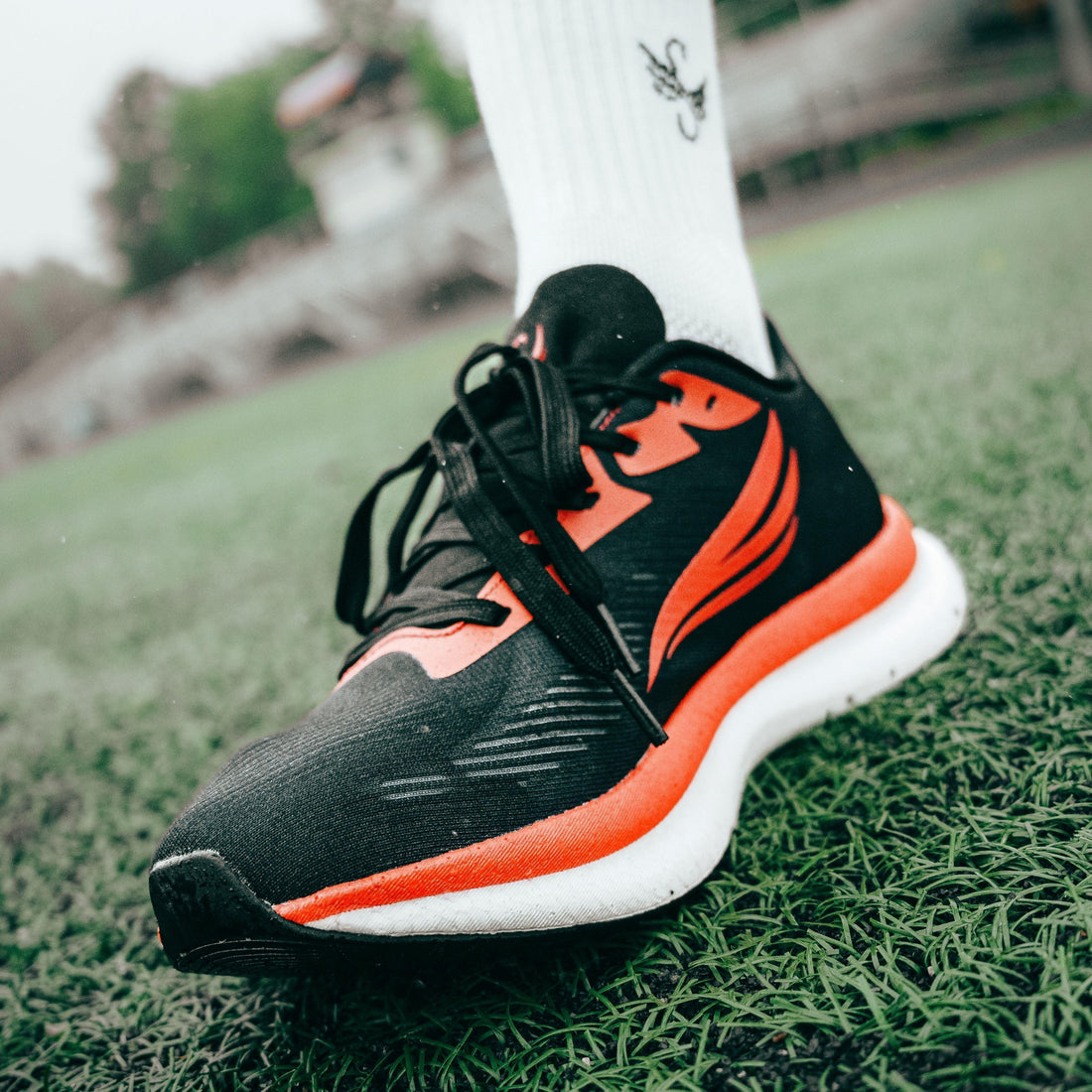 Black and orange athletic running shoe on foot, close-up on green turf field