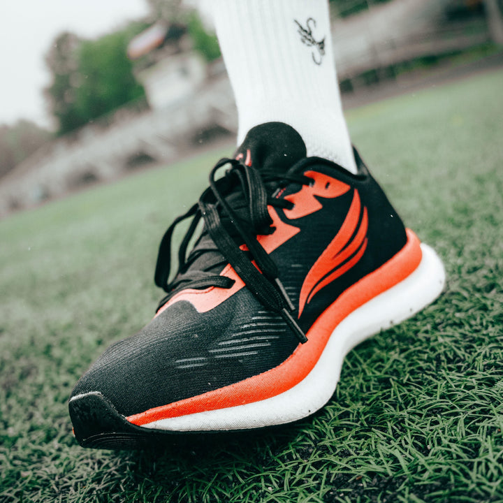 Black and orange athletic running shoe on foot, close-up on green turf field