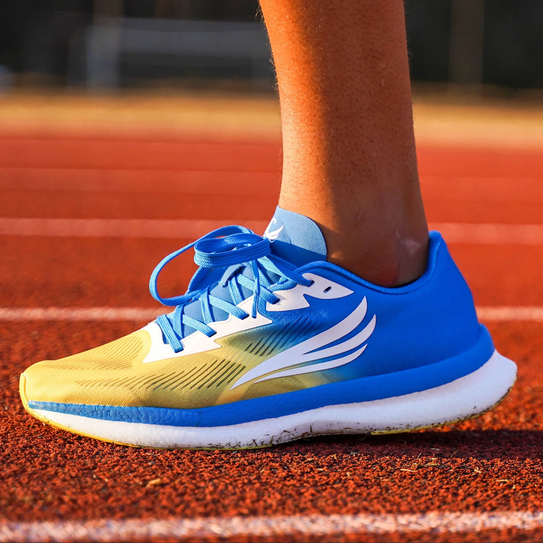 Blue and yellow athletic running shoe with wing design on a track