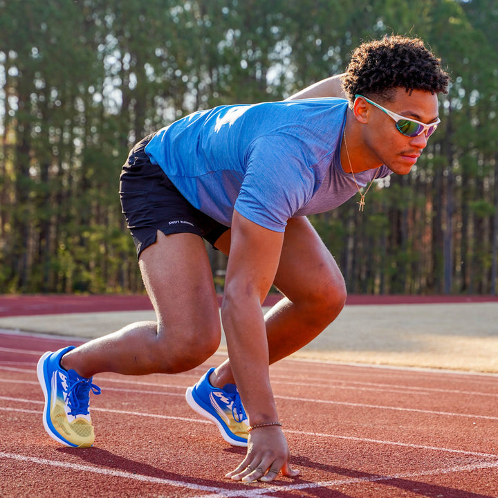 Athlete wearing blue and yellow running shoes in sprint start position on outdoor track