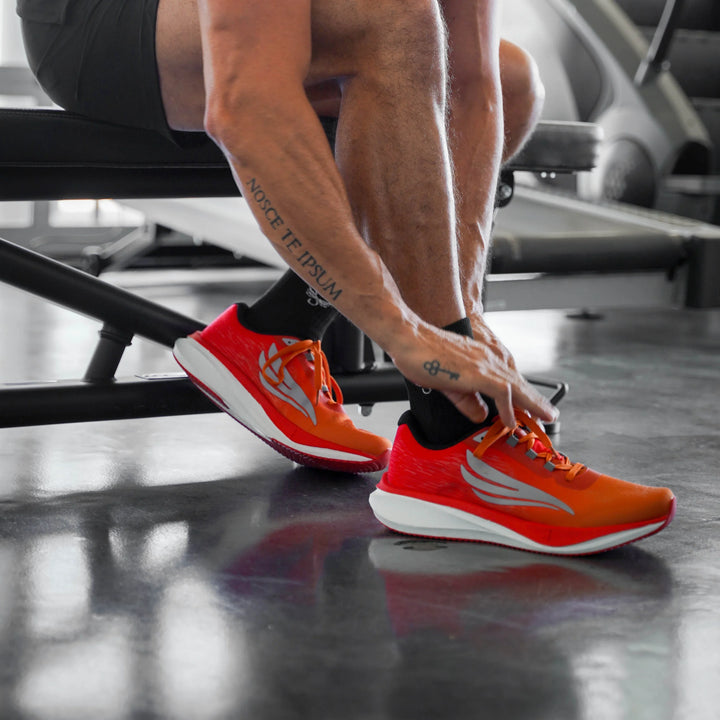 Man in gym tying bright orange athletic shoes, sitting on bench, preparing for workout