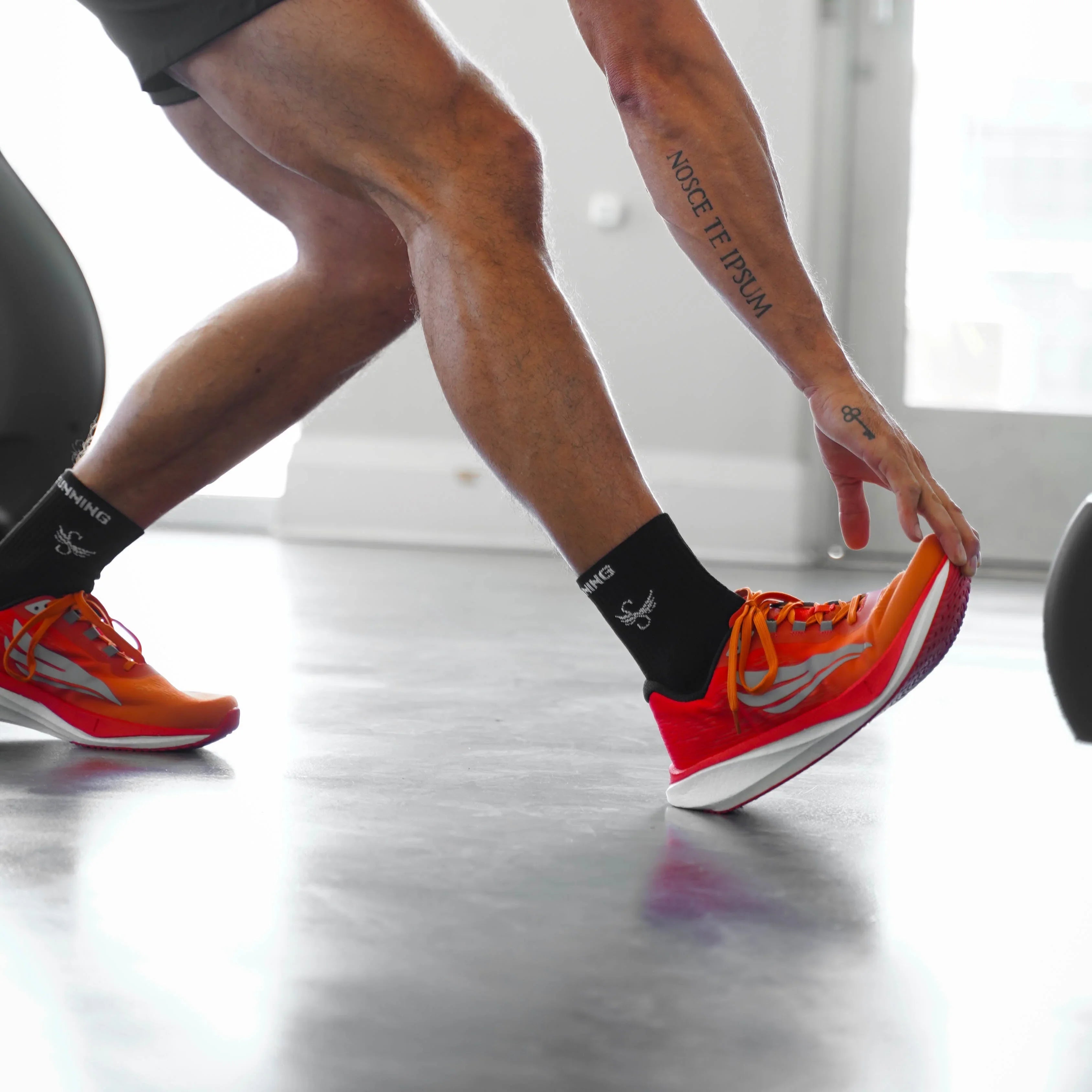 Athlete stretching indoors wearing orange athletic running shoes and black socks