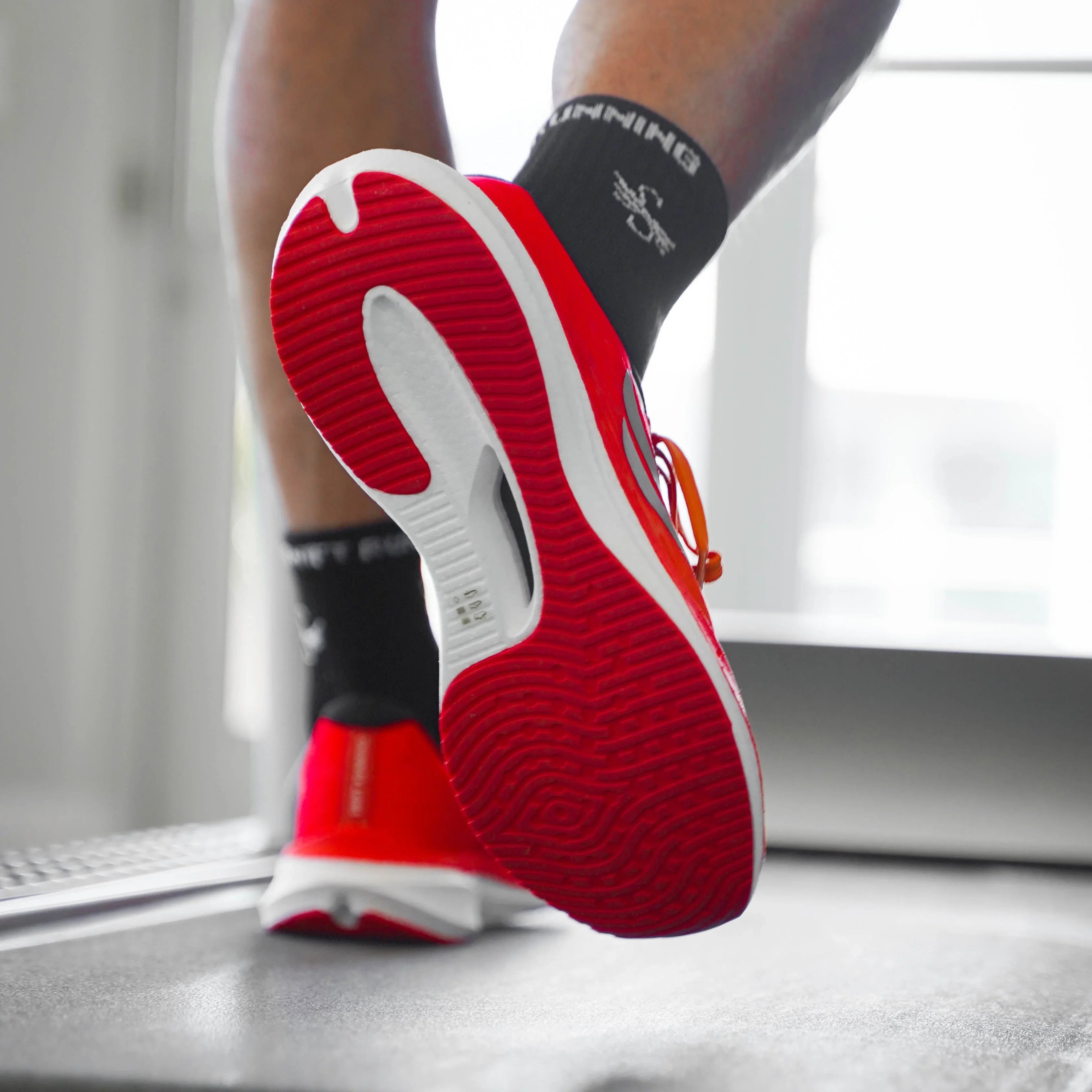 Red athletic running shoes with textured sole on treadmill in bright indoor setting