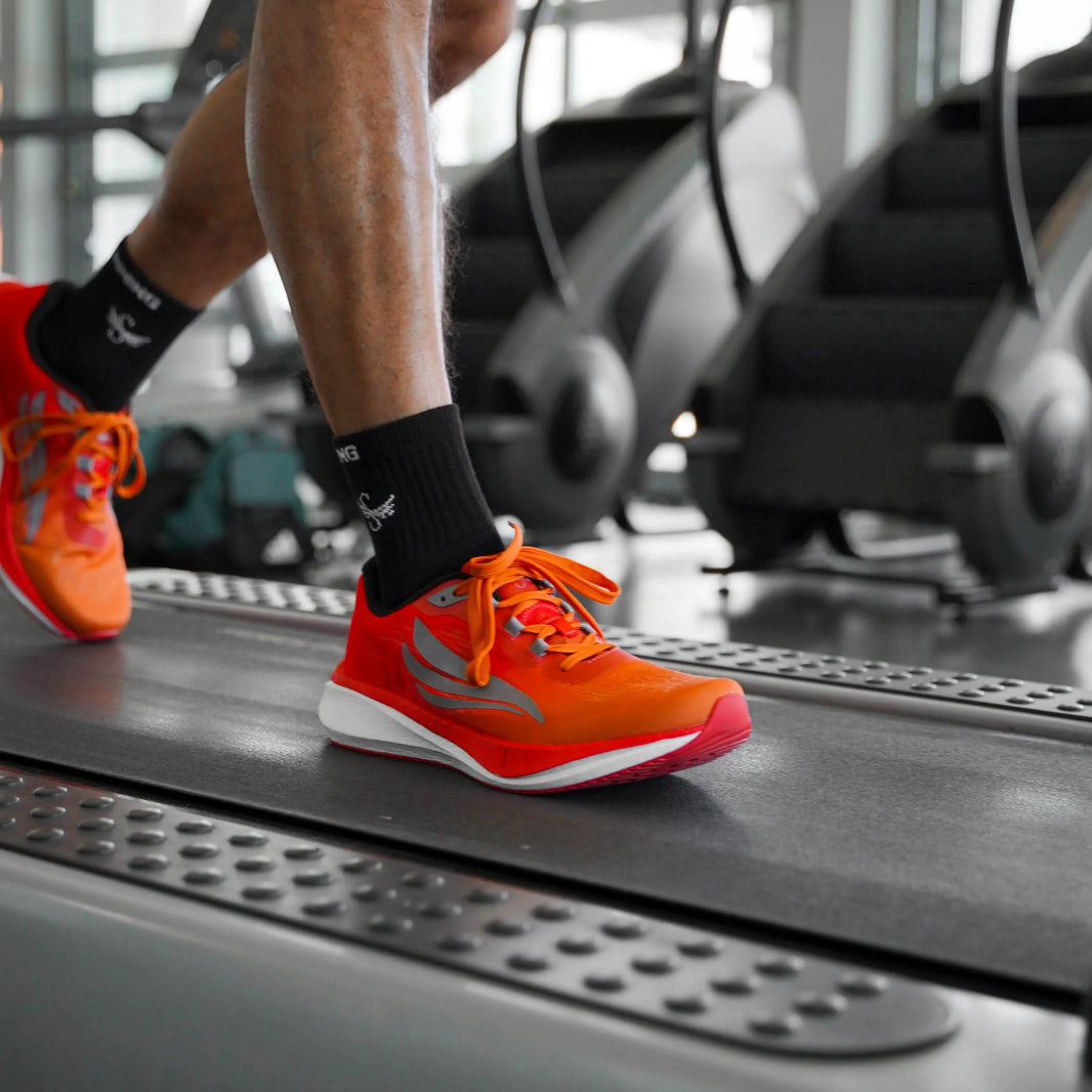 Bright orange athletic shoes on treadmill in gym, close-up of runner's legs