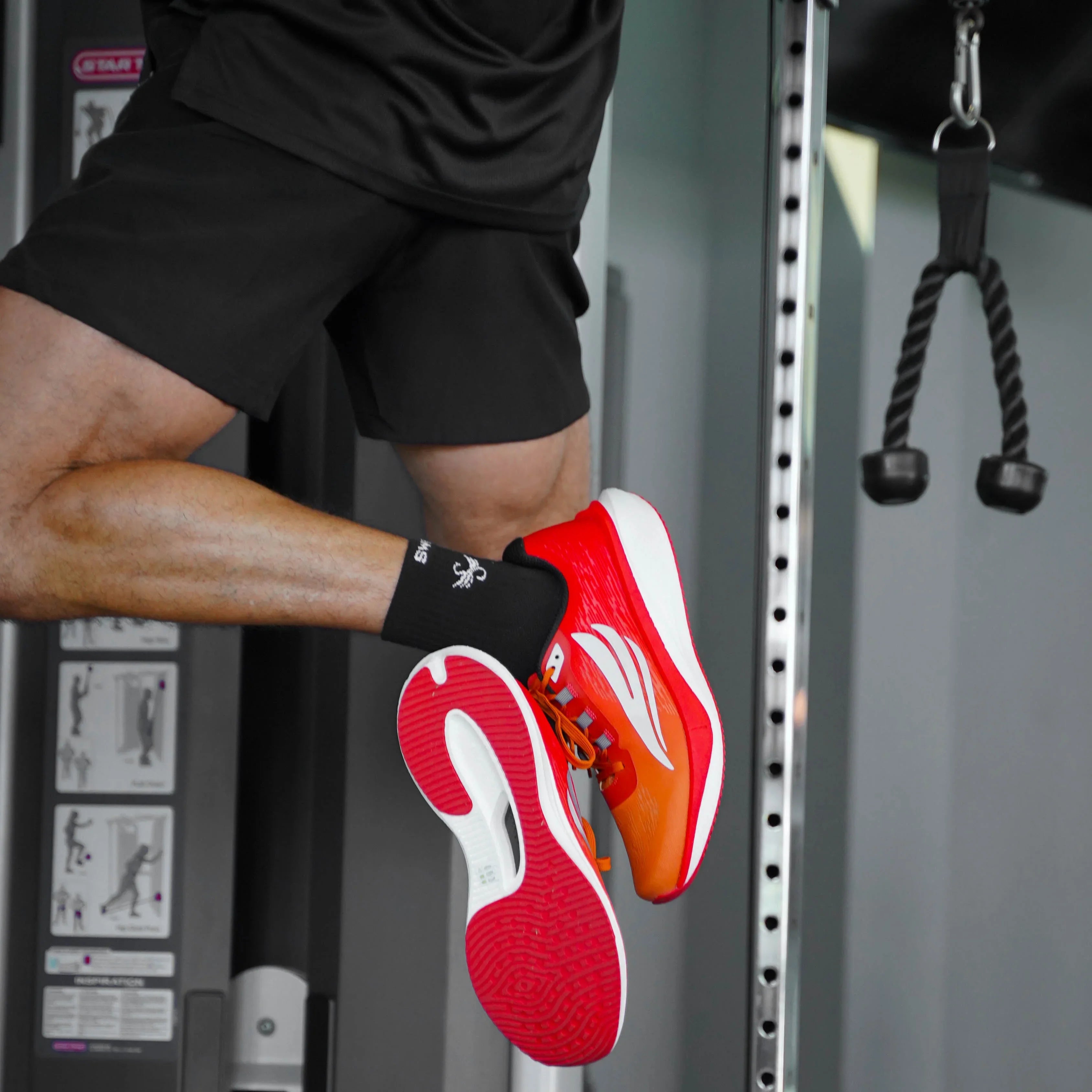 Man wearing red athletic running shoes and black shorts jumping in a gym setting