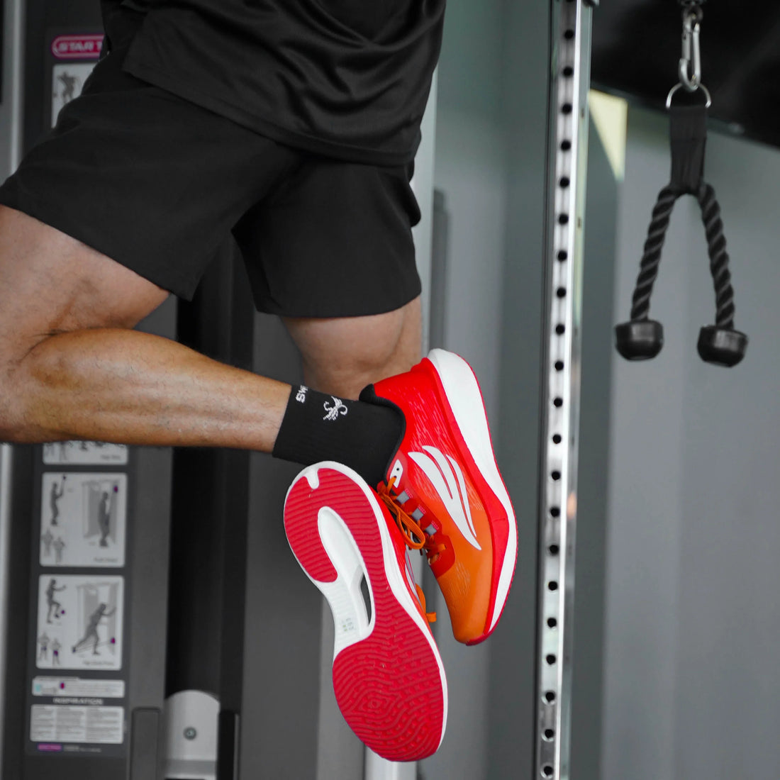 Man wearing red athletic running shoes and black shorts jumping in a gym setting