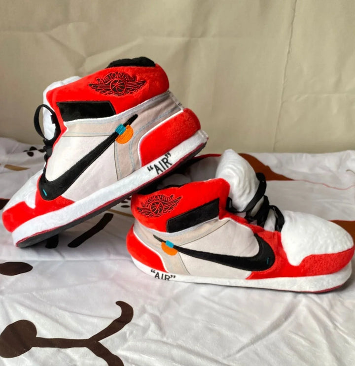 Plush sneaker slippers with red, white, and black color scheme on a bedspread