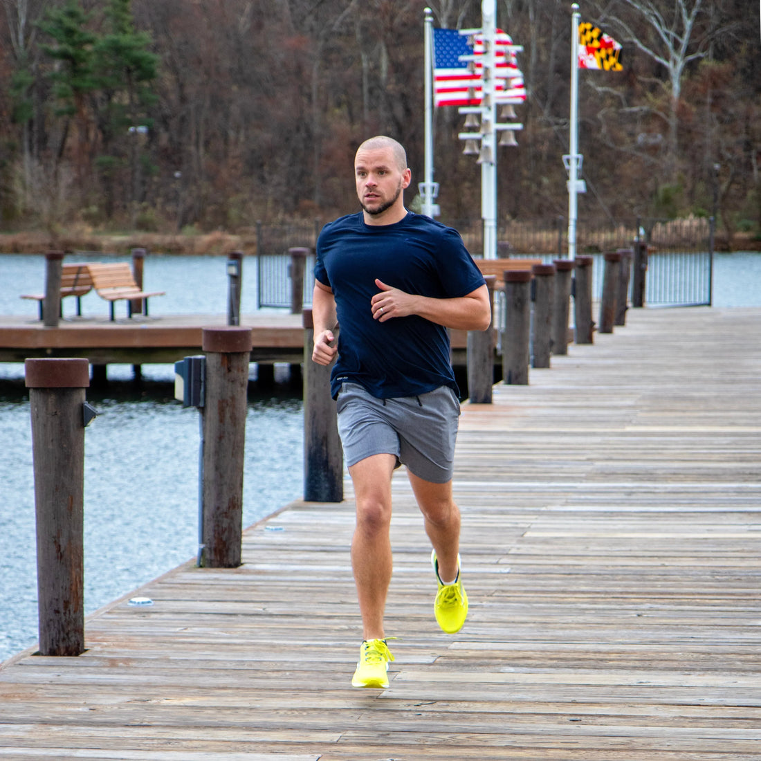 Man running on a wooden dock wearing athletic shoes, navy shirt, and gray shorts
