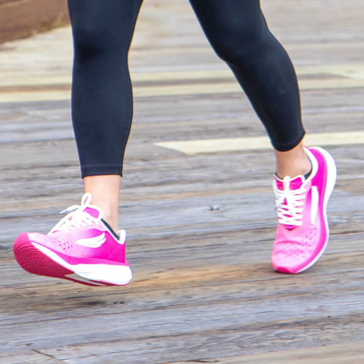 Pink athletic running shoes with white laces on a person jogging outdoors on a wooden path