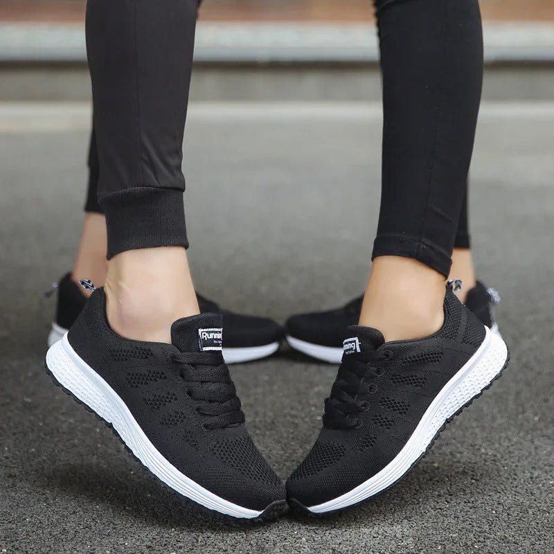 Black athletic running shoes with white soles worn outdoors on pavement