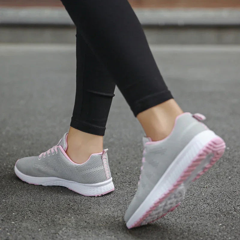 Woman walking outdoors wearing light grey athletic sneakers with pink accents